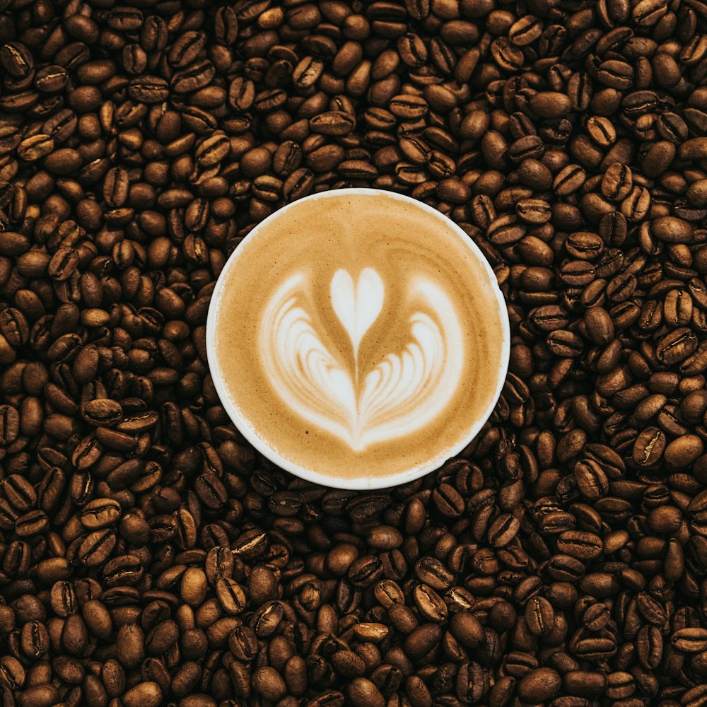 Overhead close-up of a latte heart, the cup resting in coffee beans
