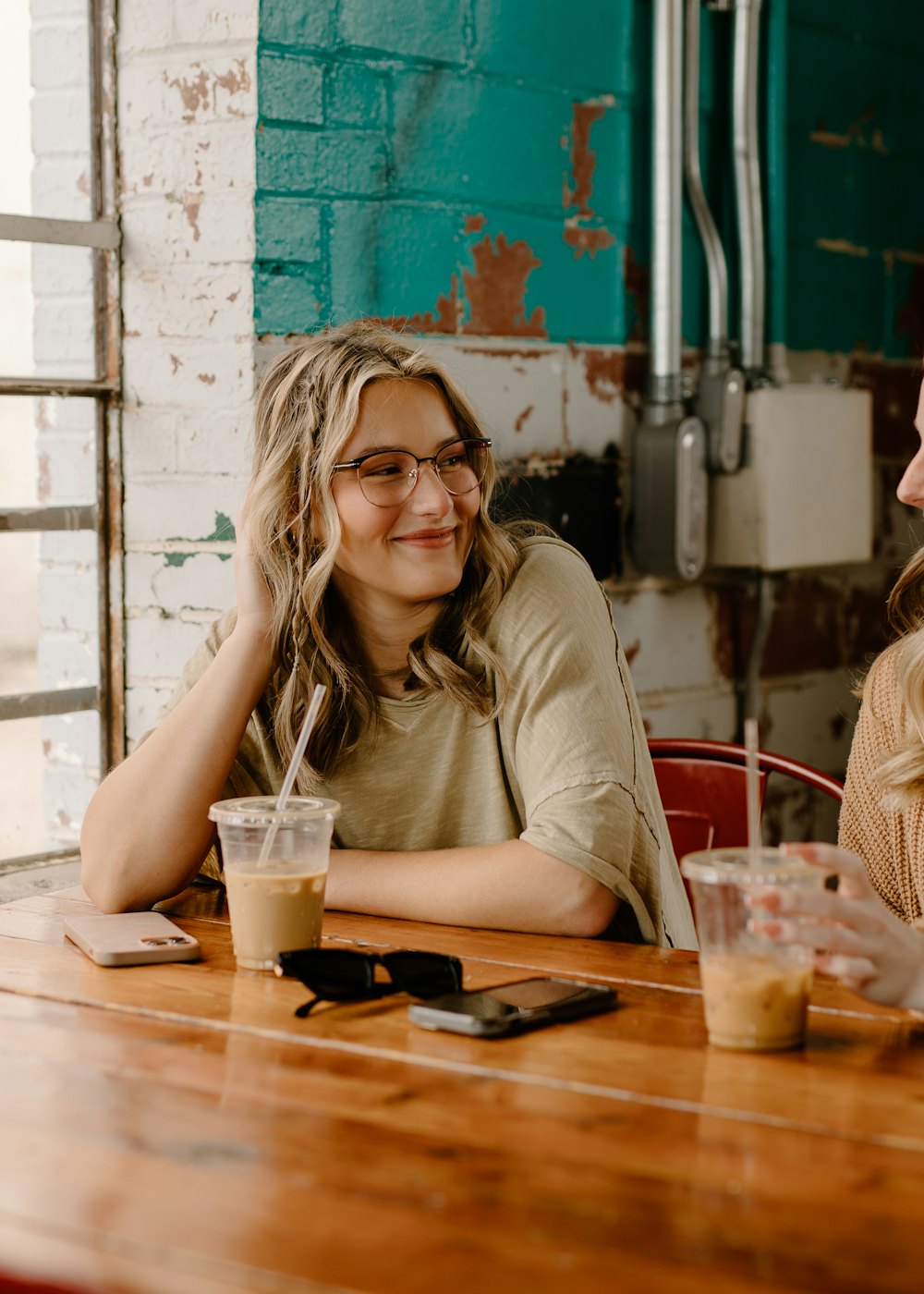 A guest smiling over iced coffees at a wooden café table