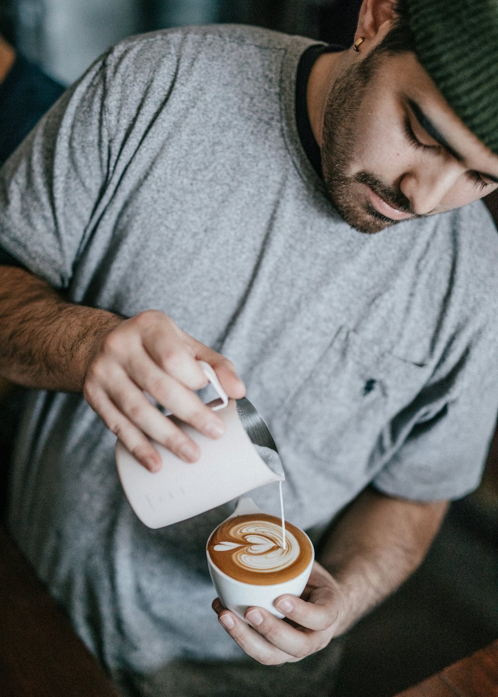 A barista finishing a cappuccino, milk jug in hand