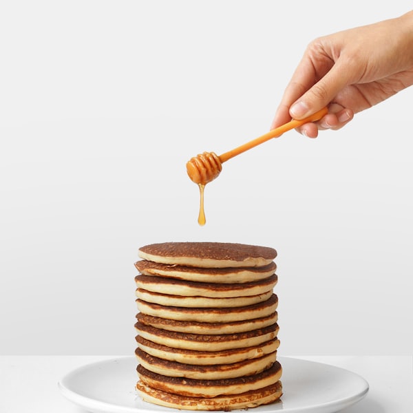 Pancakes with honey trailing from a wooden dipper