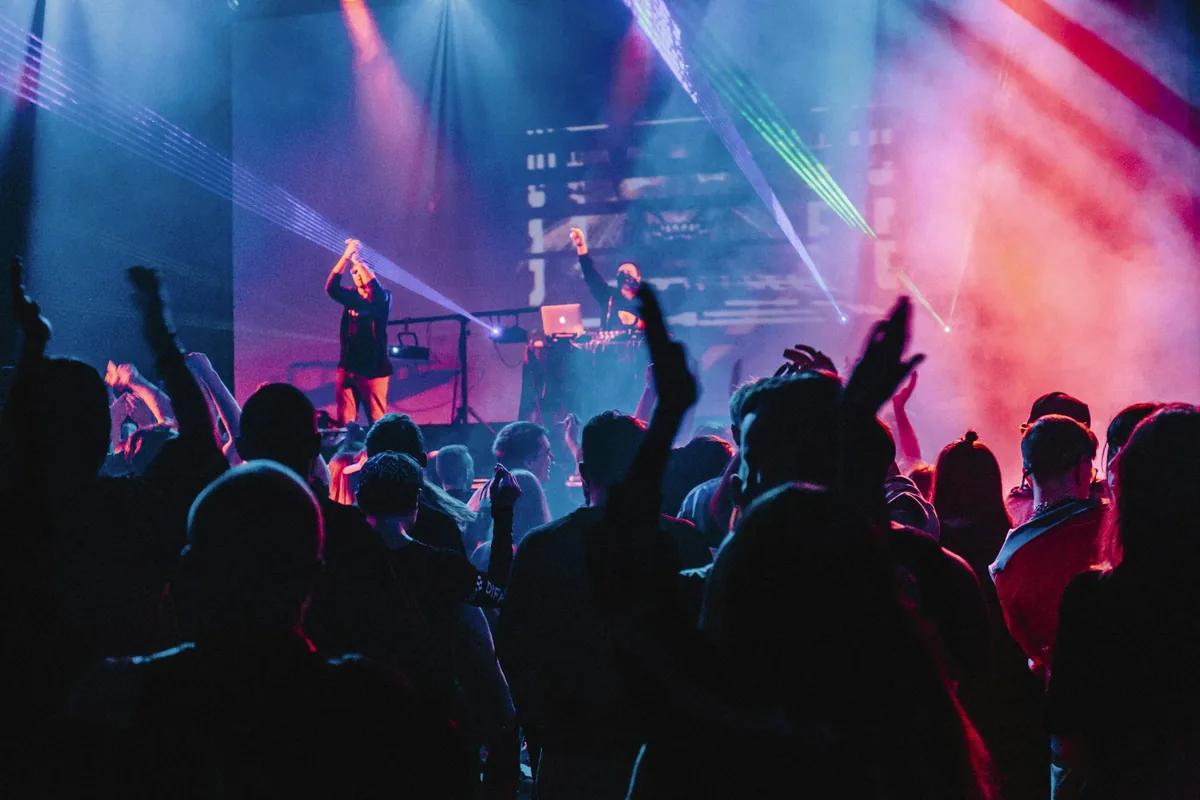 Crowd with raised hands lit by pink stage light