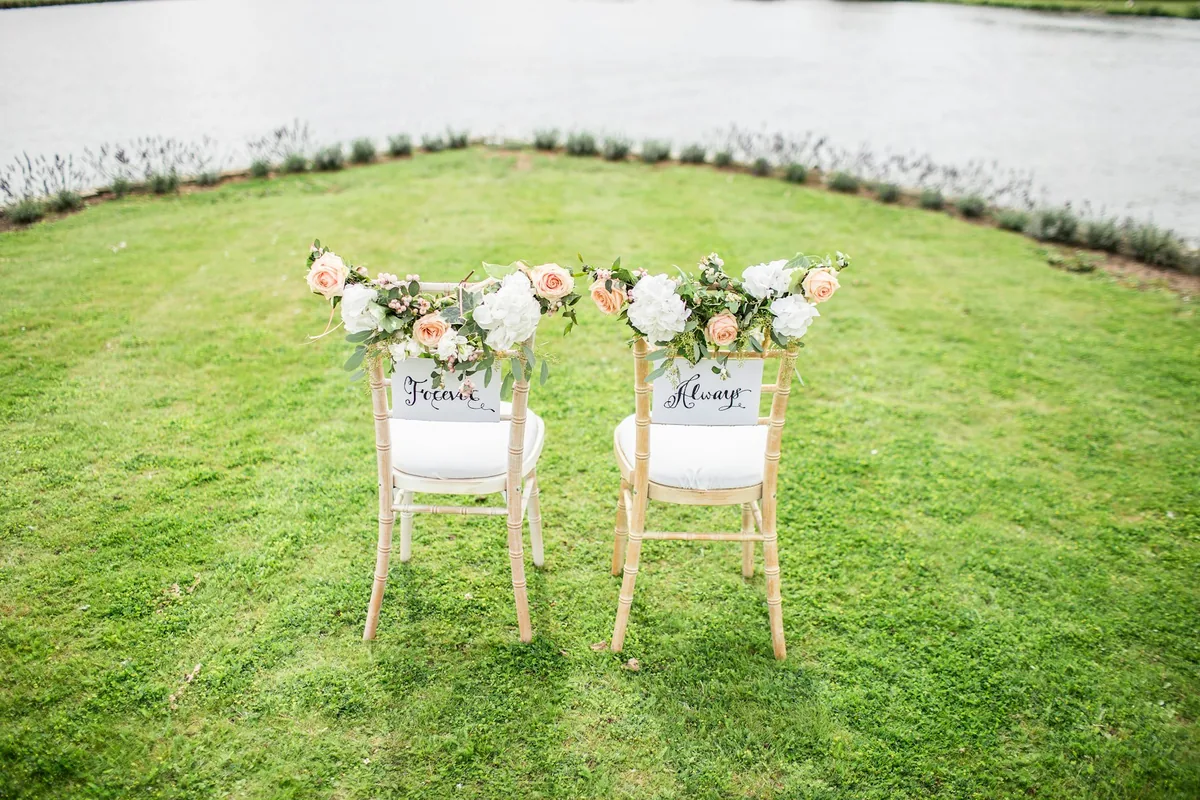 Two ceremony chairs decorated with flowers on a lawn