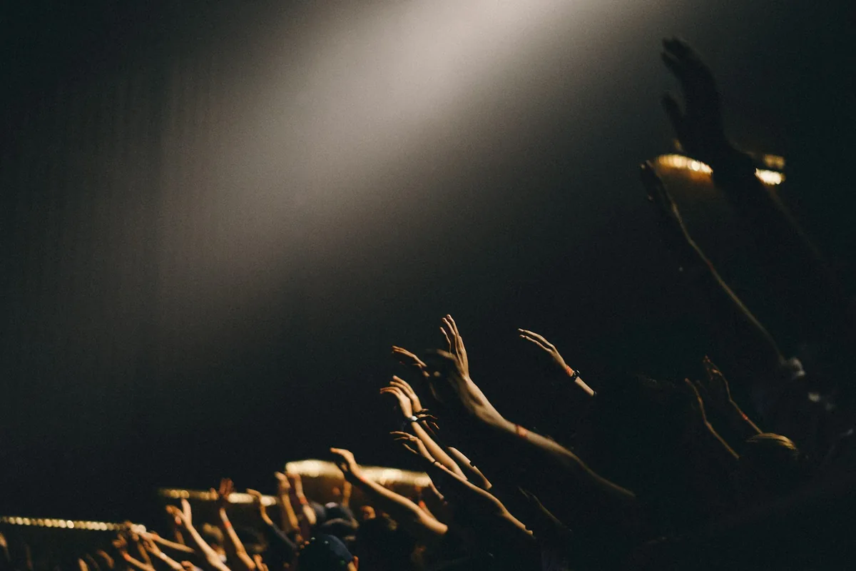 Hands raised in golden light in a dark venue