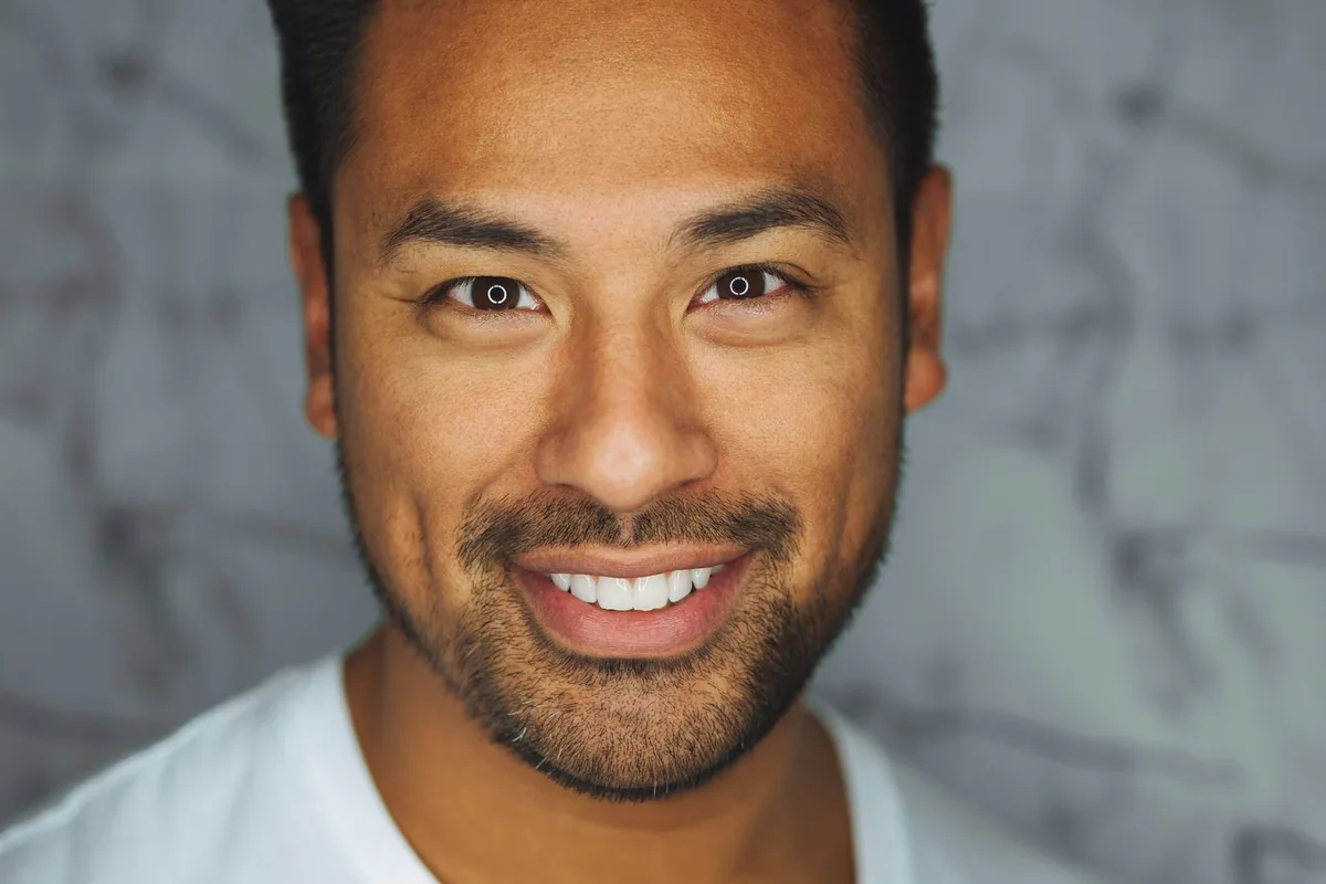 Studio headshot of a smiling man against a concrete wall