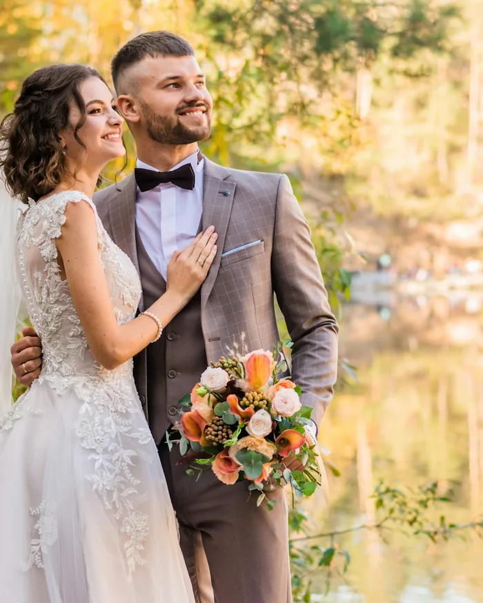 Newlyweds laughing beside a lake in autumn light