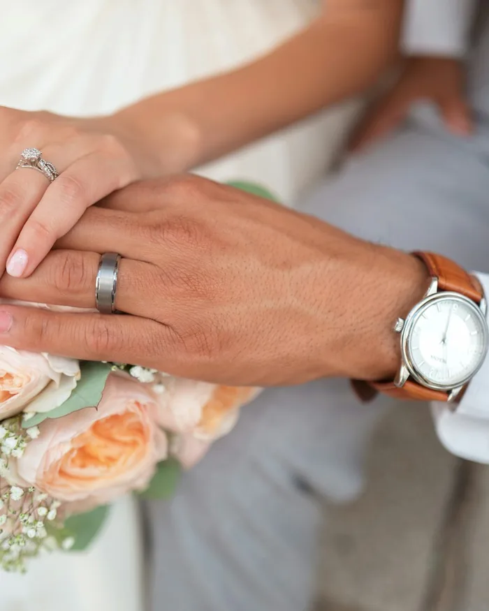 Detail of the couple's hands and wedding rings over a bouquet