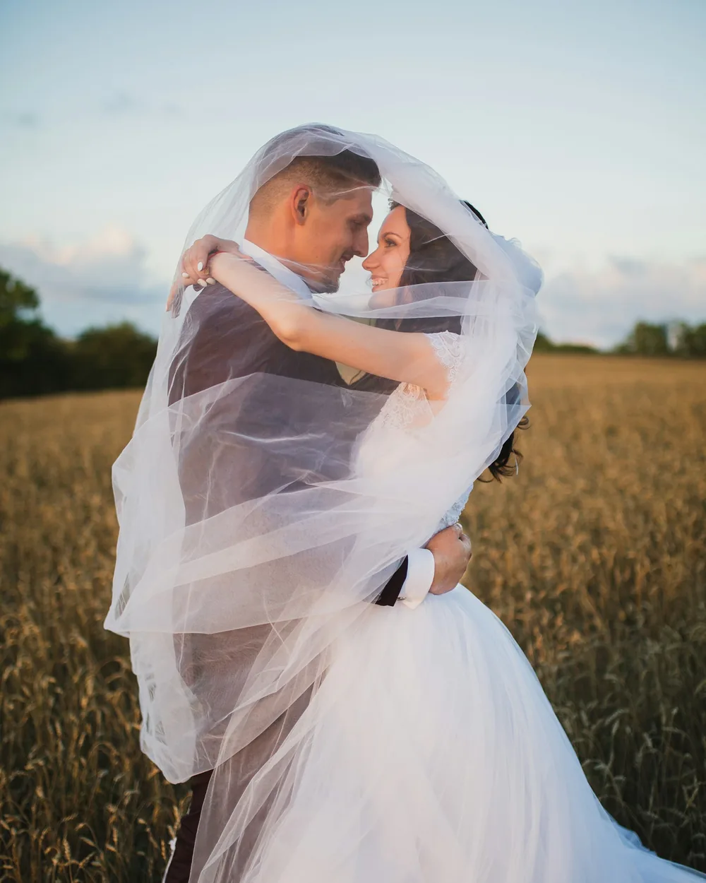 Couple embracing beneath a floating veil in a wheat field