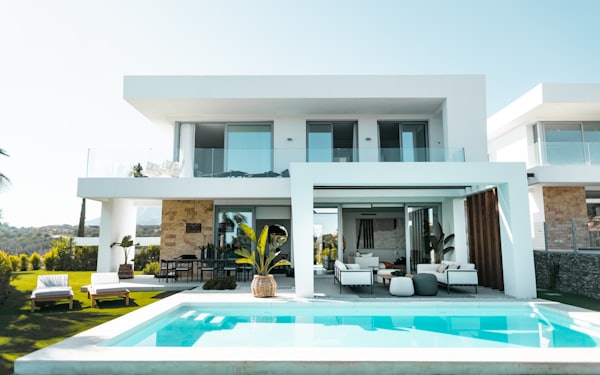 A white flat-roofed villa with a rectangular swimming pool and an outdoor lounge area