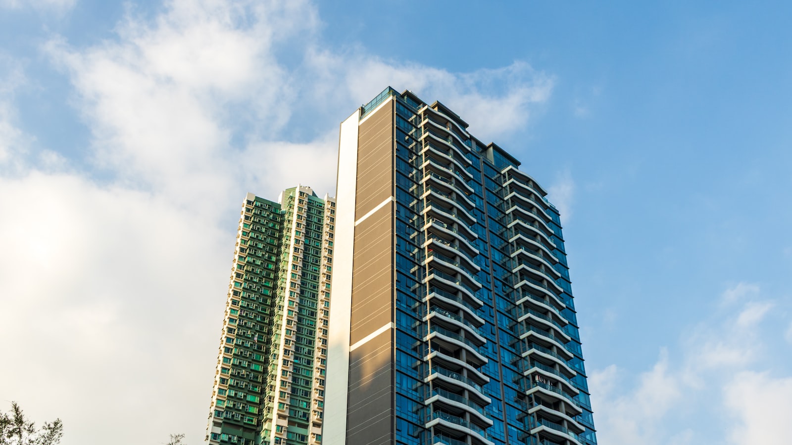 Two modern high-rise apartment towers with pale facades rising against a blue sky scattered with white cloud