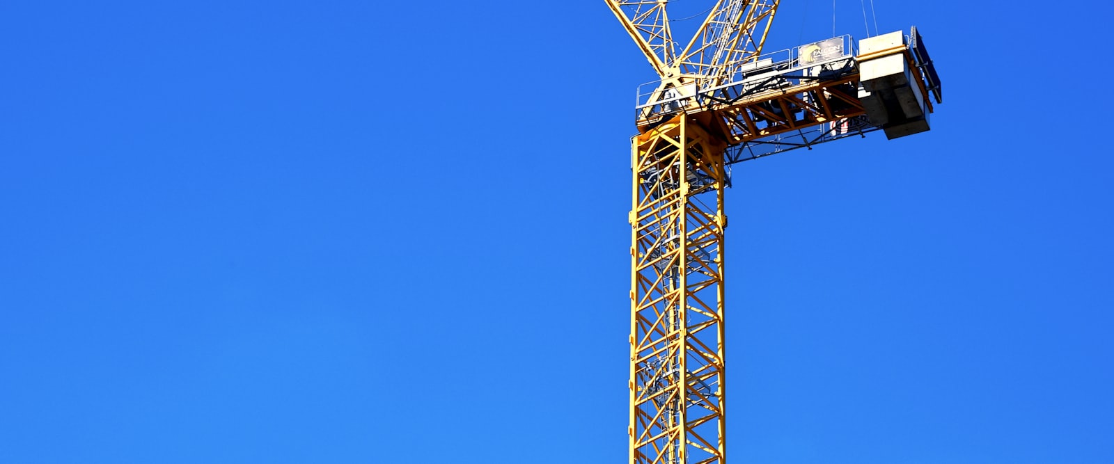 A tower crane standing over a new development, its jib crossing an open blue sky
