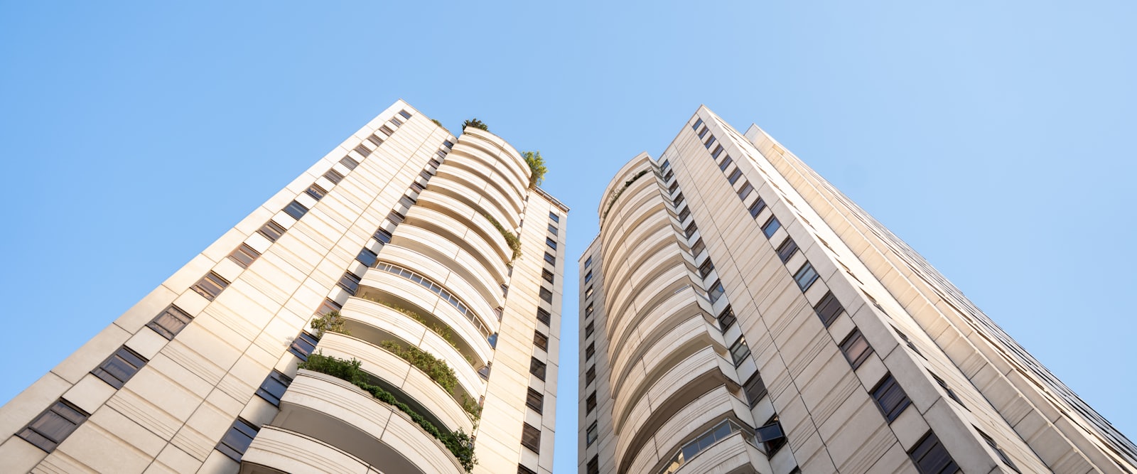 Two tall contemporary residential buildings photographed from below against a clear blue sky