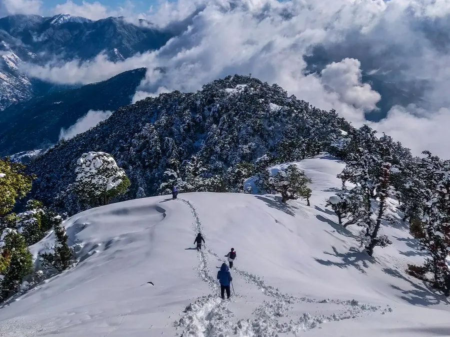 Trekkers crossing a snowfield below Himalayan peaks near Manali