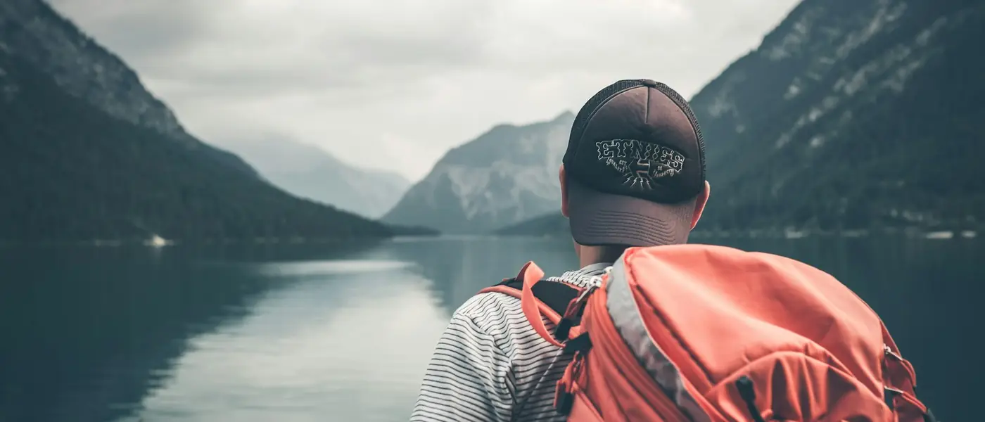 Traveller with a backpack looking out over a mountain lake